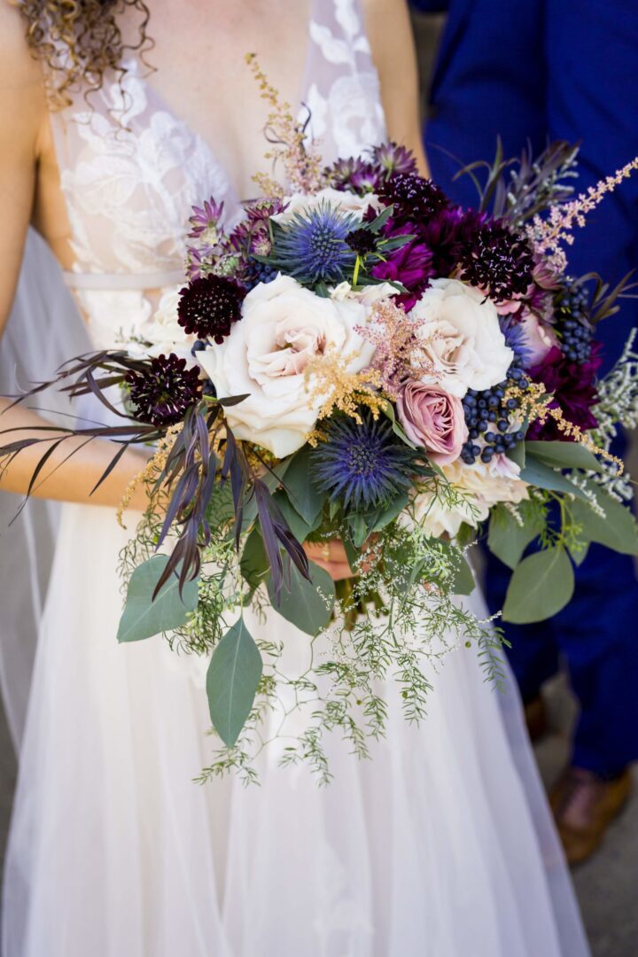 A bride is holding a bouquet of purple flowers.