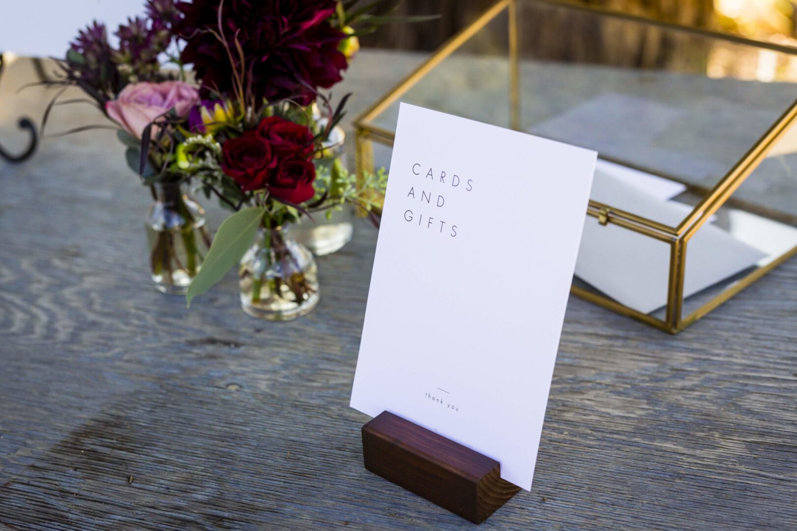 A wooden place card holder on a table with flowers.