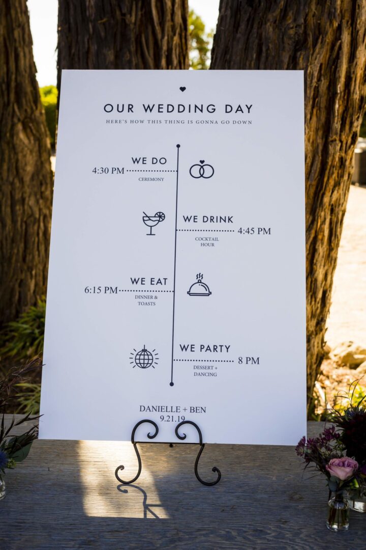 A wedding day timeline sign in front of a tree.