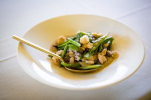 A white plate with green beans and chicken in it.