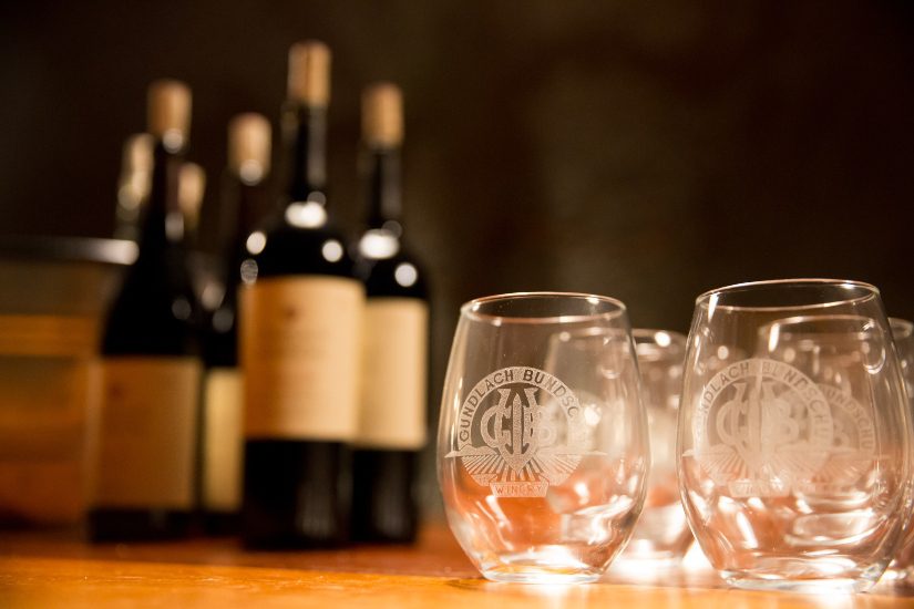 Wine glasses on a table with bottles of wine.