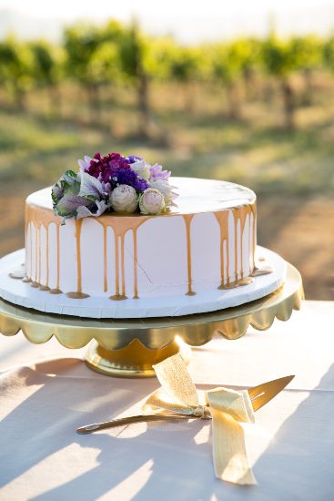 A wedding cake is sitting on a table in front of a vineyard.