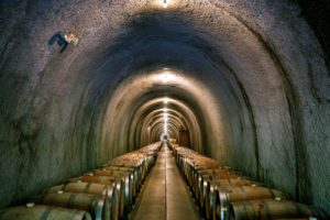 A wine cellar with rows of barrels lined up in a tunnel.