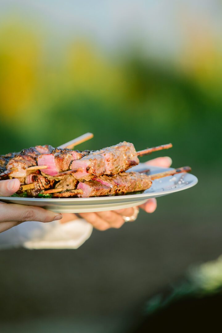 A person holding a plate of meat on skewers.