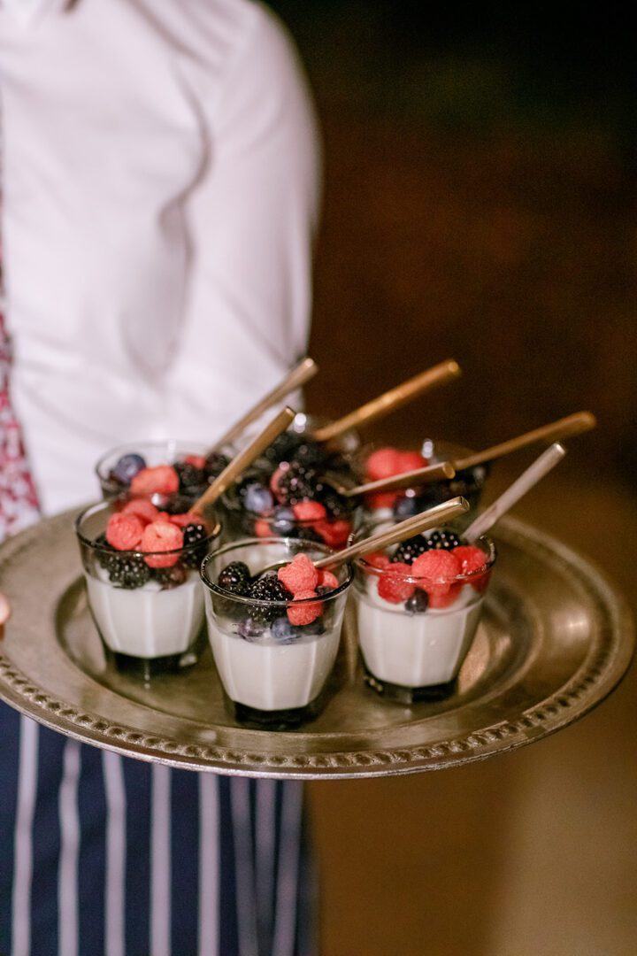A waiter is holding a tray of desserts with berries on it.