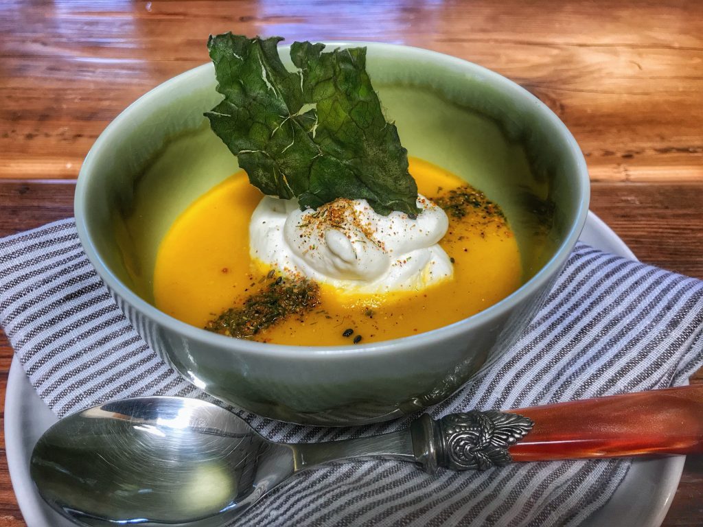 A bowl of soup with sour cream and kale.