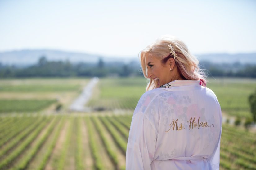 A woman wearing a robe in front of a vineyard.