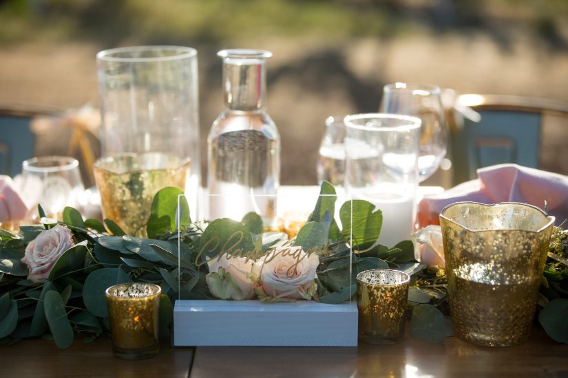 A table setting with vases, candles and greenery.