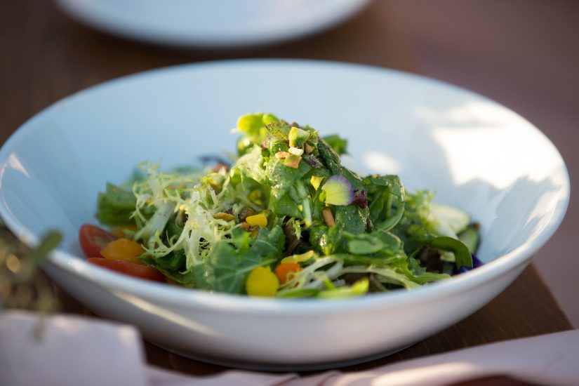 A salad in a white bowl on a wooden table.