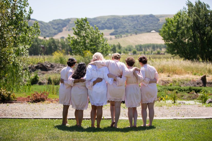 A group of bridesmaids in pink robes standing in a field.