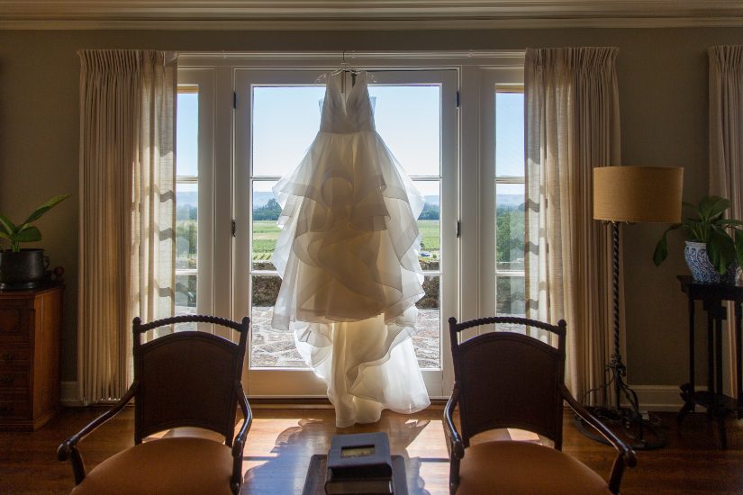 A wedding dress hangs in front of a window.