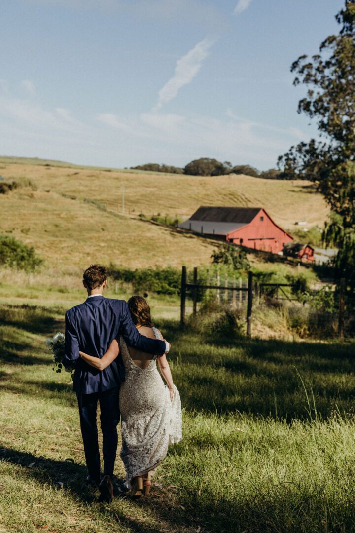 A bride and groom walking down a path with a red barn in the background.