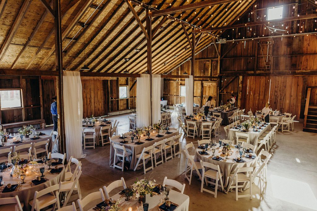 A wedding reception in a barn with white tables and chairs.