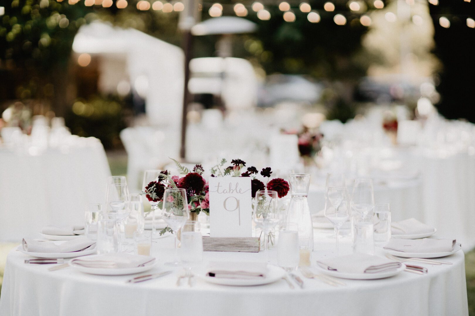 A white table setting with burgundy place settings.