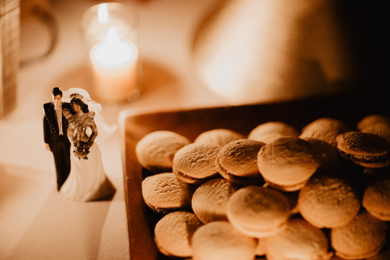 Macaroons and a figurine of a bride and groom in front of a candle.