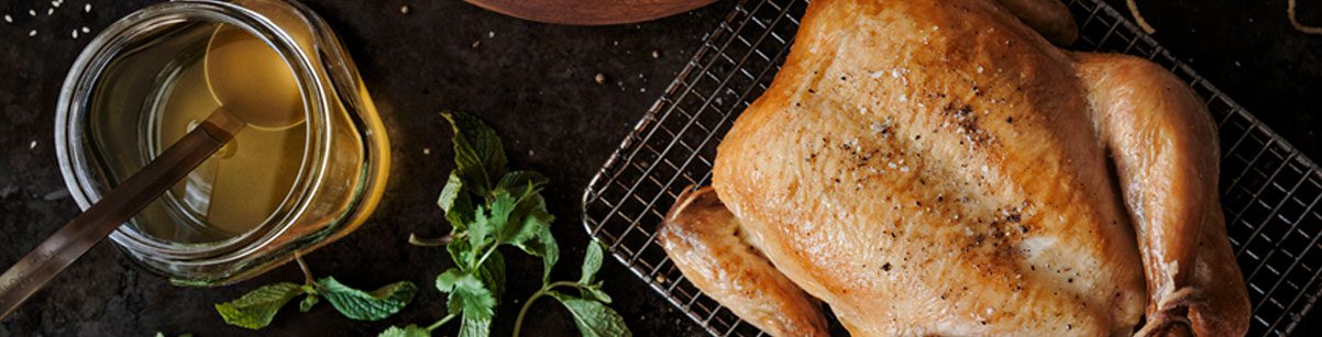 A chicken is sitting on a rack with herbs and a bottle of honey.