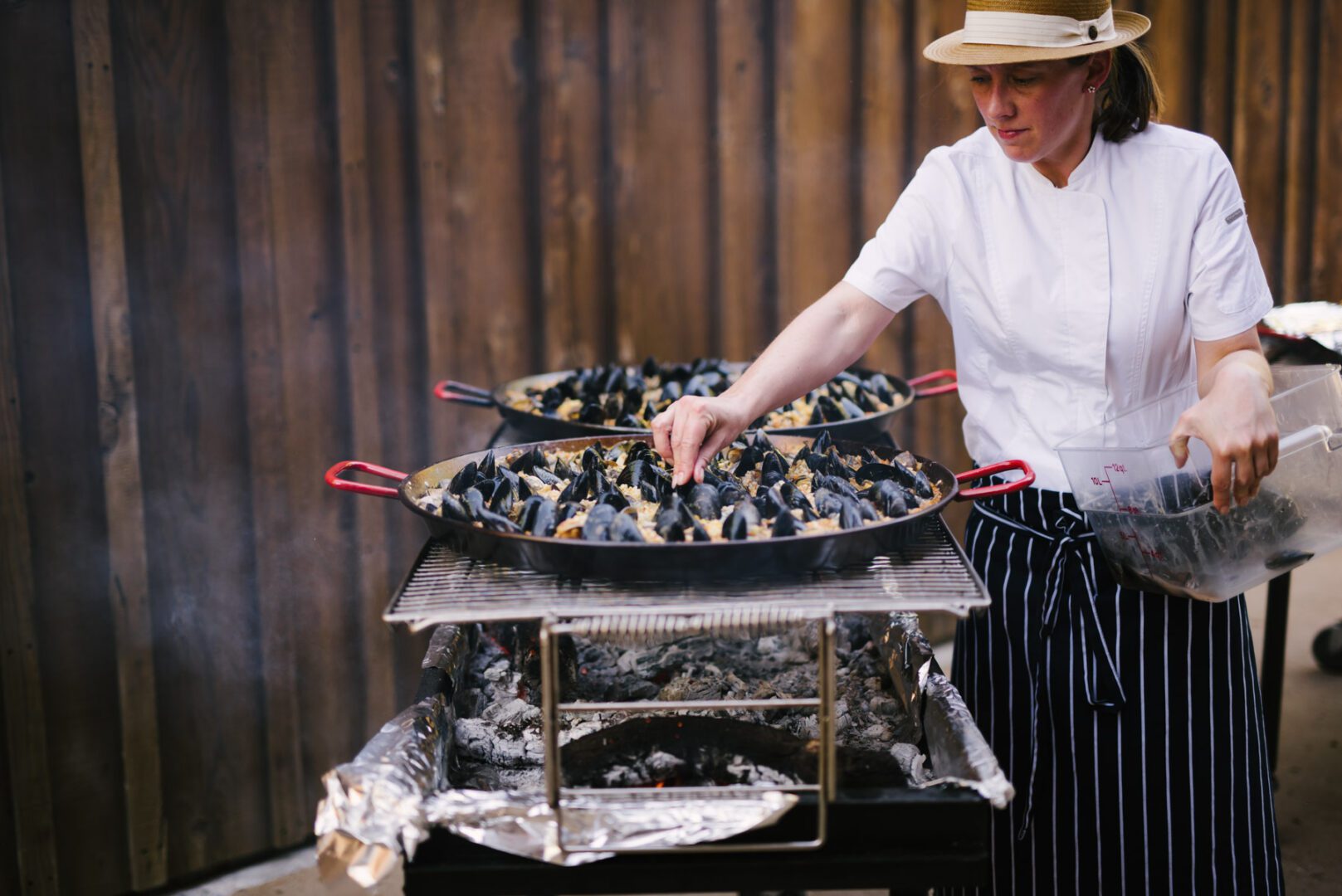 A woman is preparing mussels on a grill.