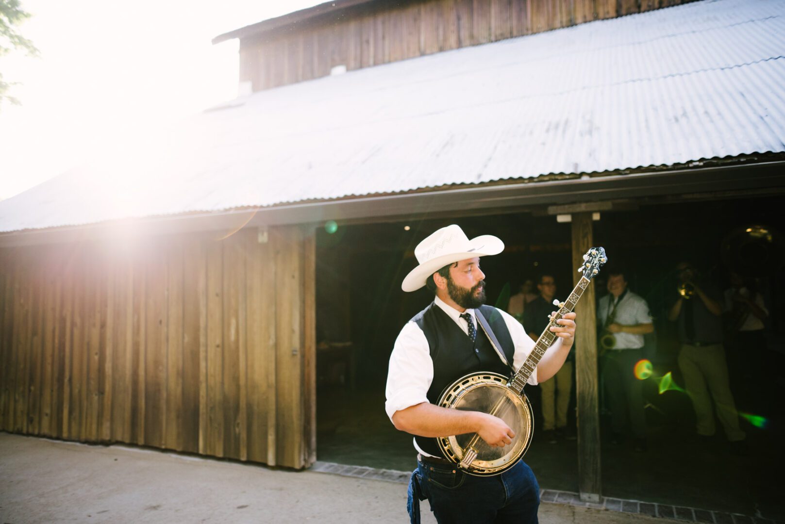 A man playing a banjo in front of a barn.
