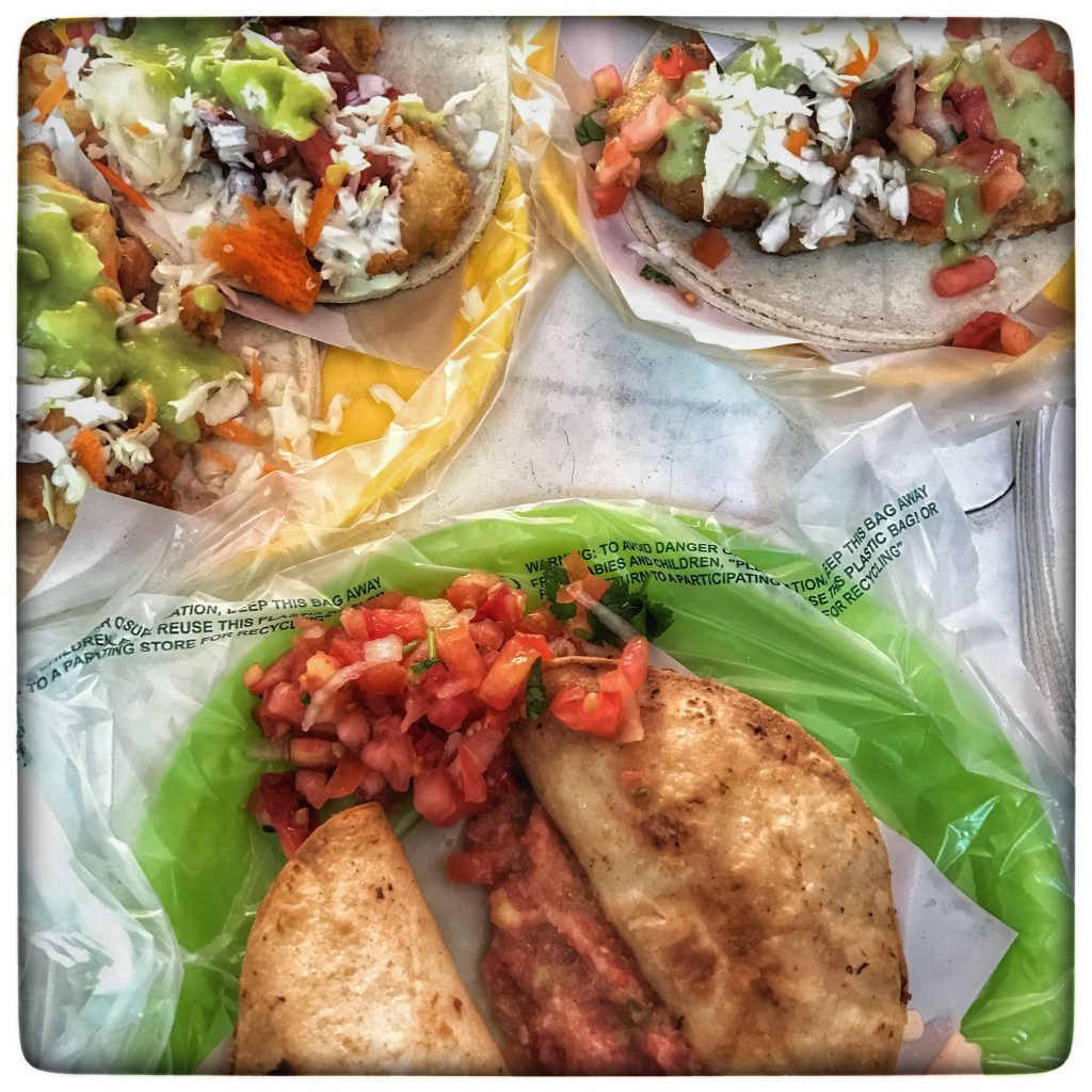 Three tacos on a plate with vegetables and salsa.