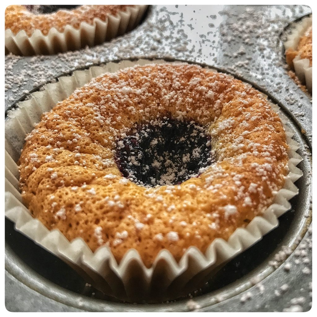 Blueberry muffins in a muffin tin with powdered sugar.