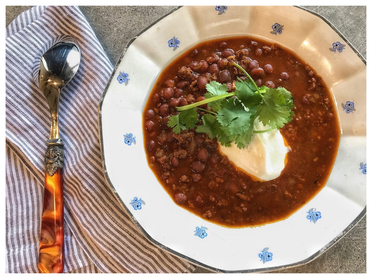 A bowl of chili with sour cream and a spoon.