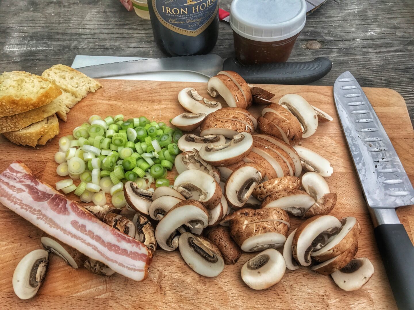 A cutting board with bacon, mushrooms, onions and bread.