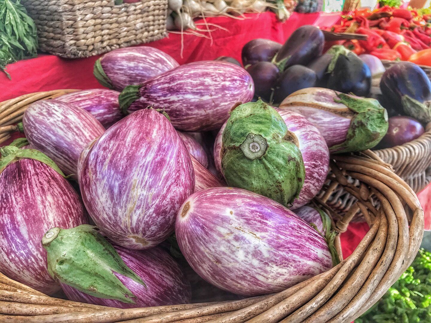 Purple eggplants in a basket on a table at a farmers' market.