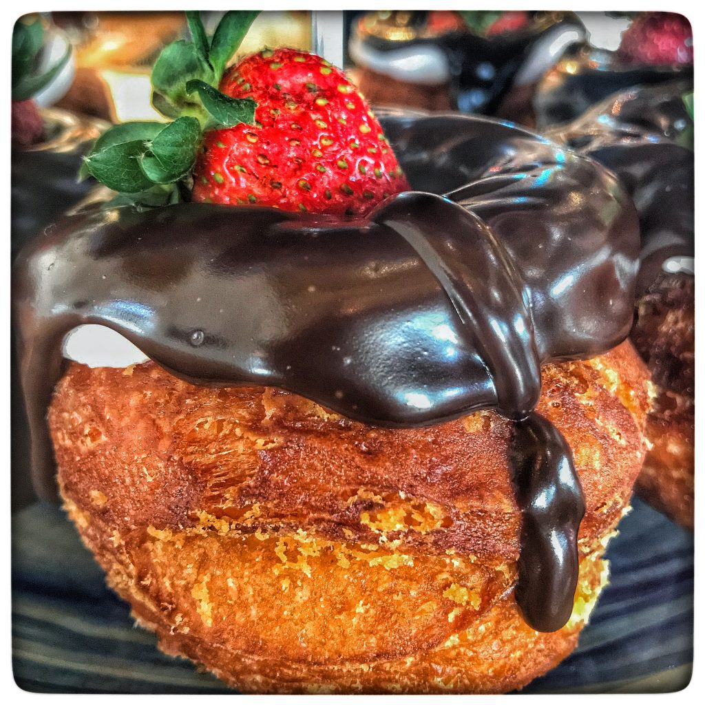 A chocolate dipped donut with a strawberry on top.