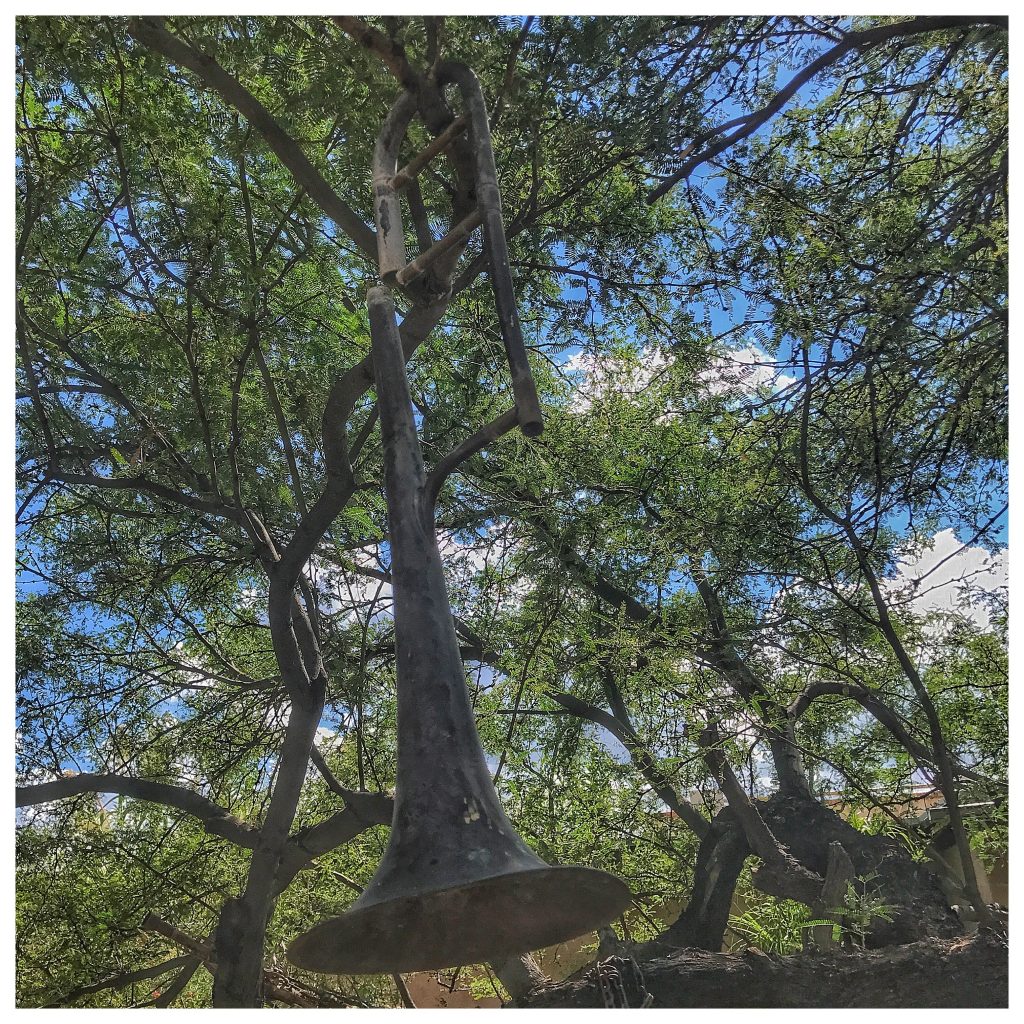 A metal trumpet hanging from a tree.