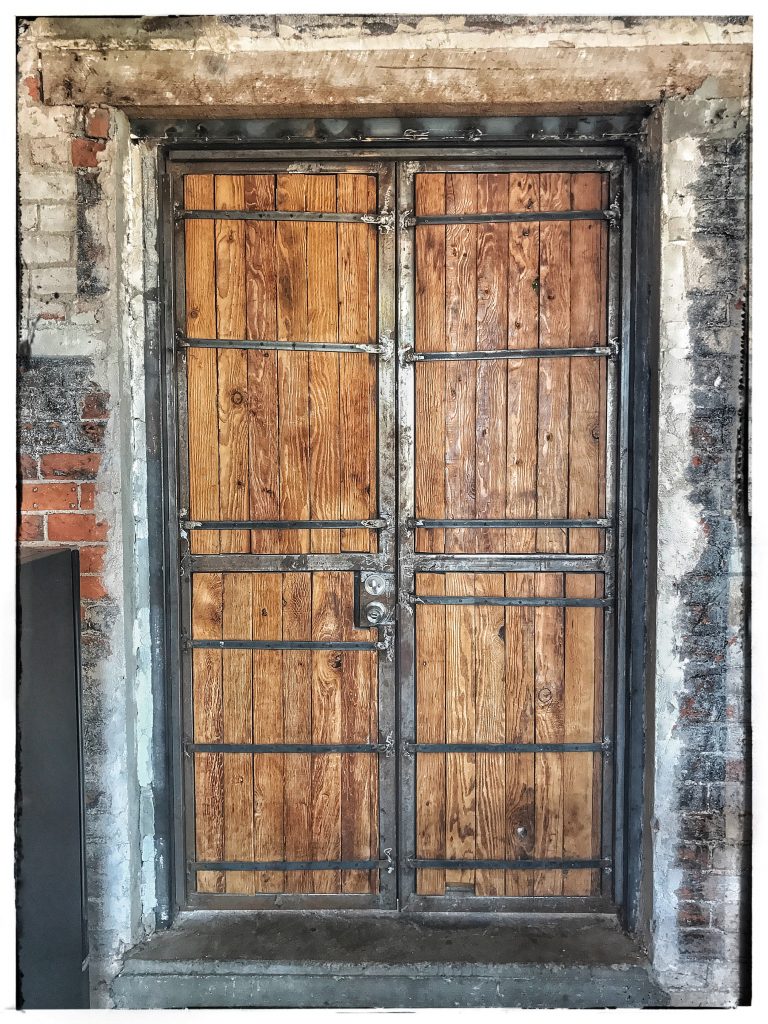 A wooden door with metal bars and a brick wall.