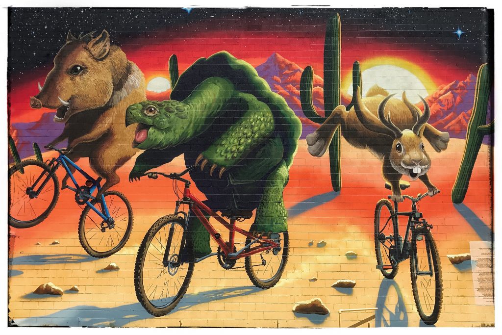 A mural depicting a group of animals riding bicycles in the desert.