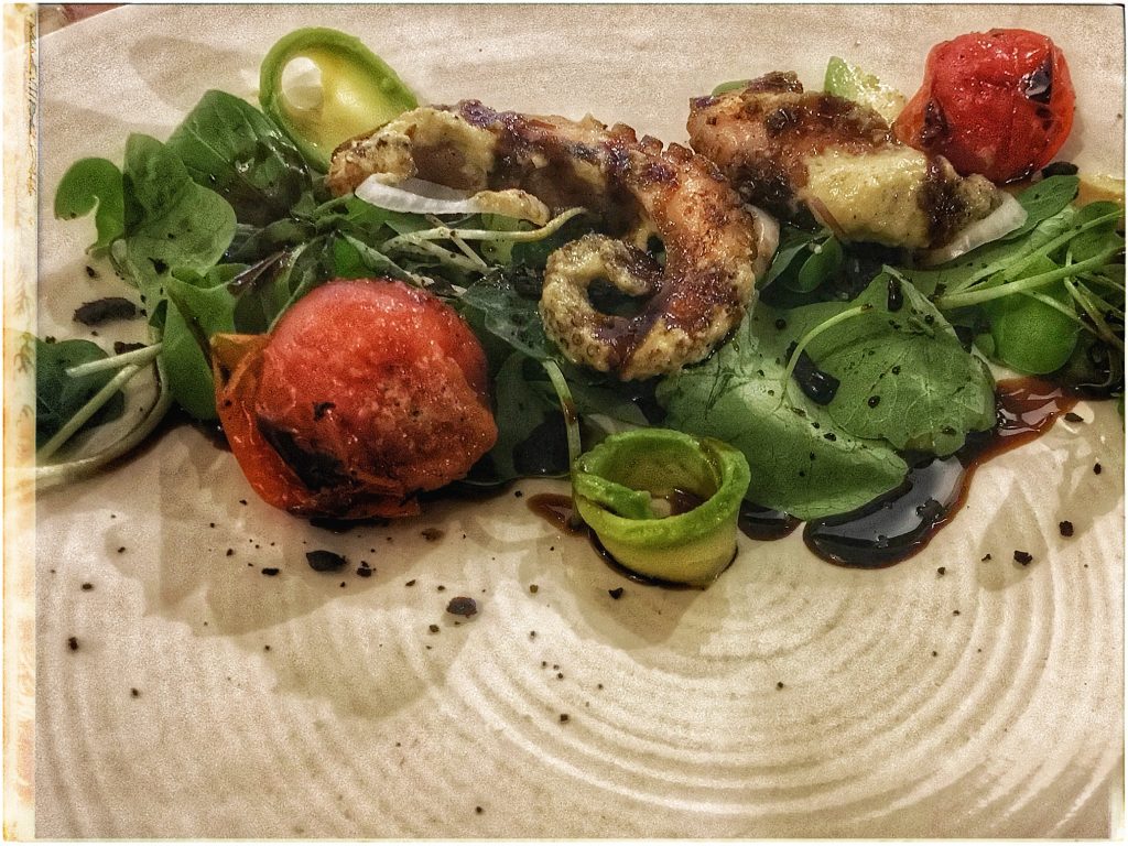 An octopus salad with tomatoes and greens on a plate.