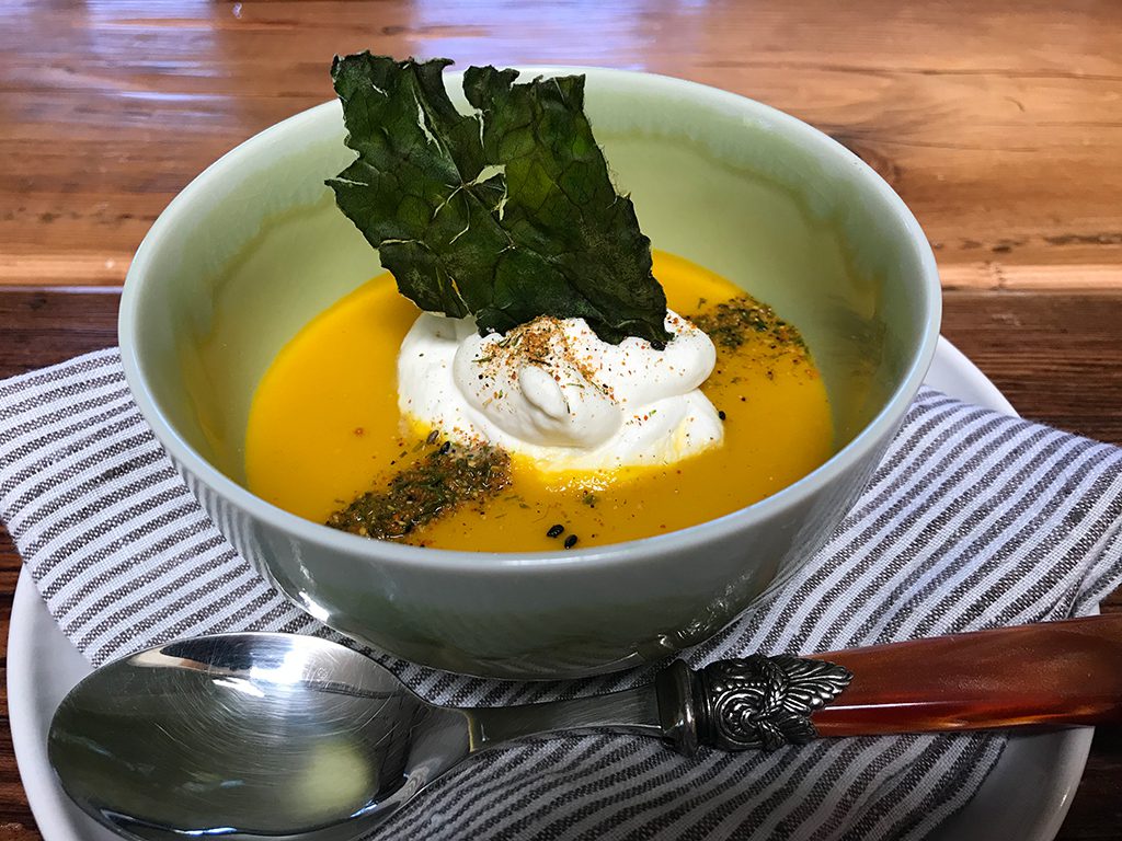 A bowl of soup with sour cream and kale.