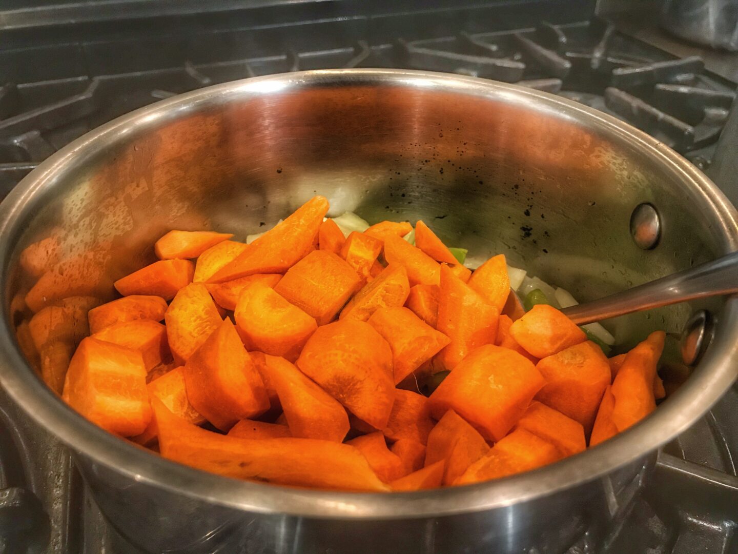 A pot filled with carrots and onions on a stove.