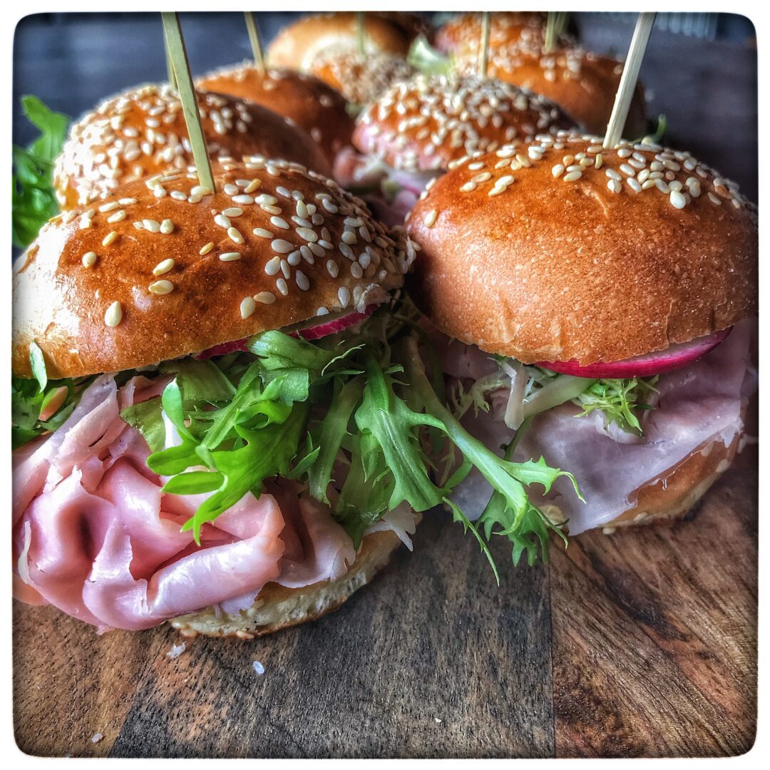 Ham sliders with radishes on a wooden board.