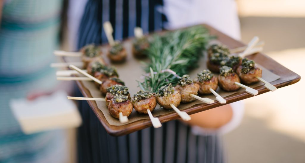 A person holding a tray of food on skewers.
