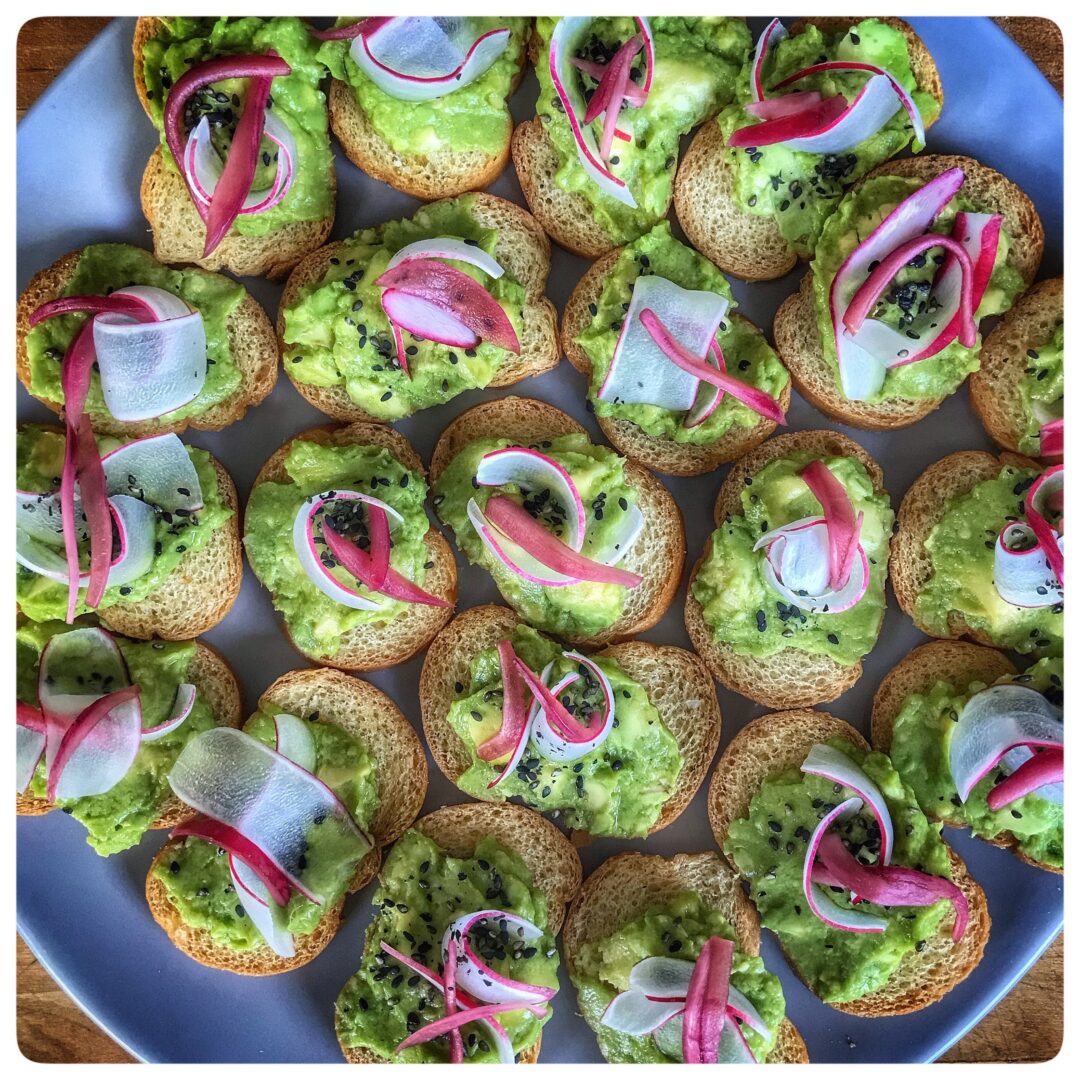 Guacamole crostini with radishes on a plate.