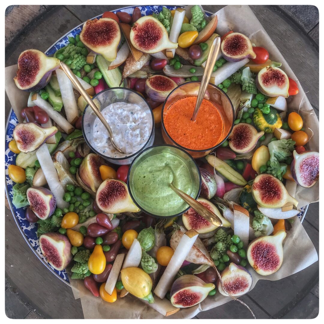 A plate with figs, vegetables and dip on it.