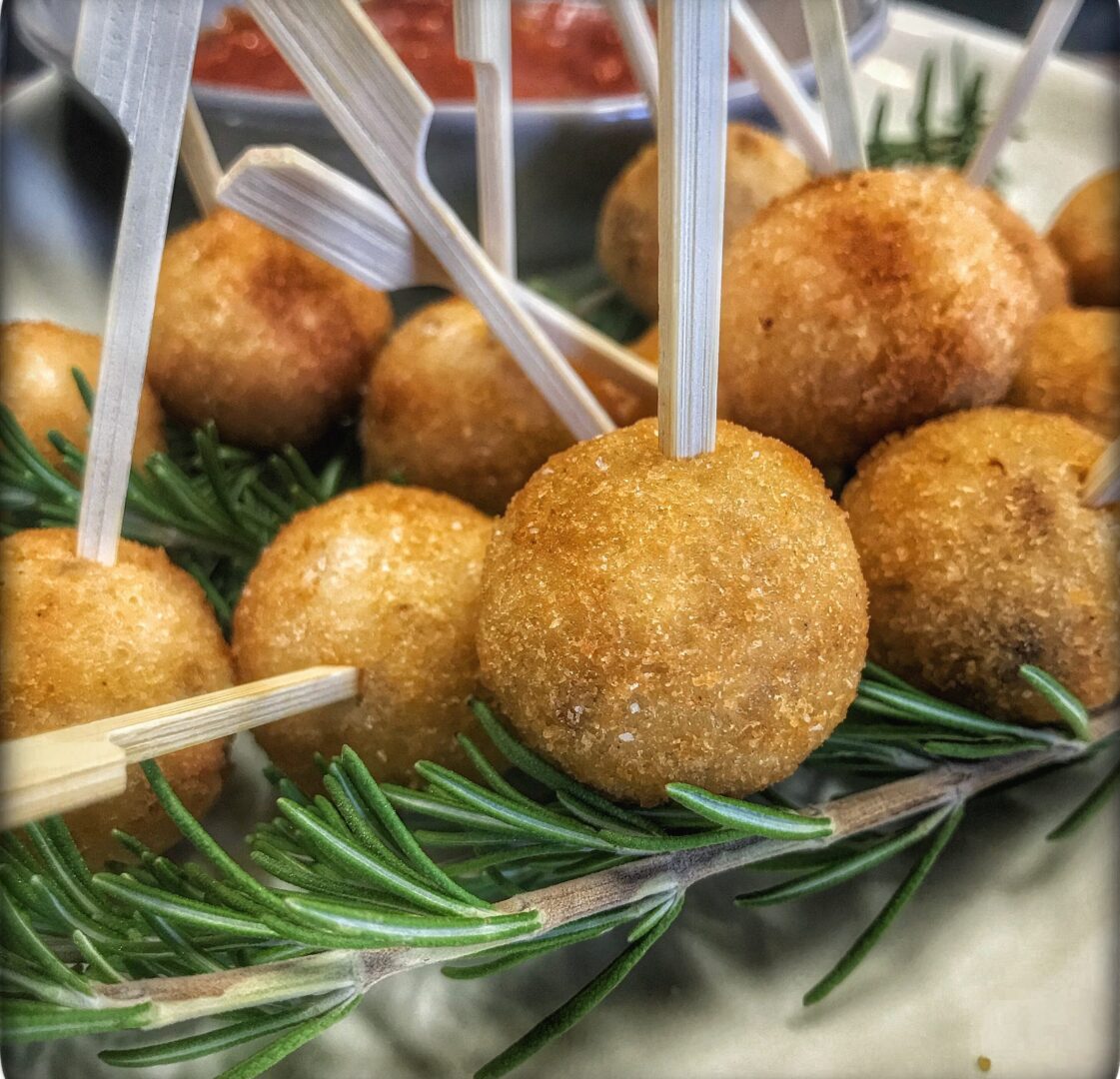A plate of meatballs on toothpicks with a rosemary sprig.