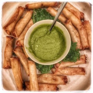 A plate of spring rolls with a green sauce.