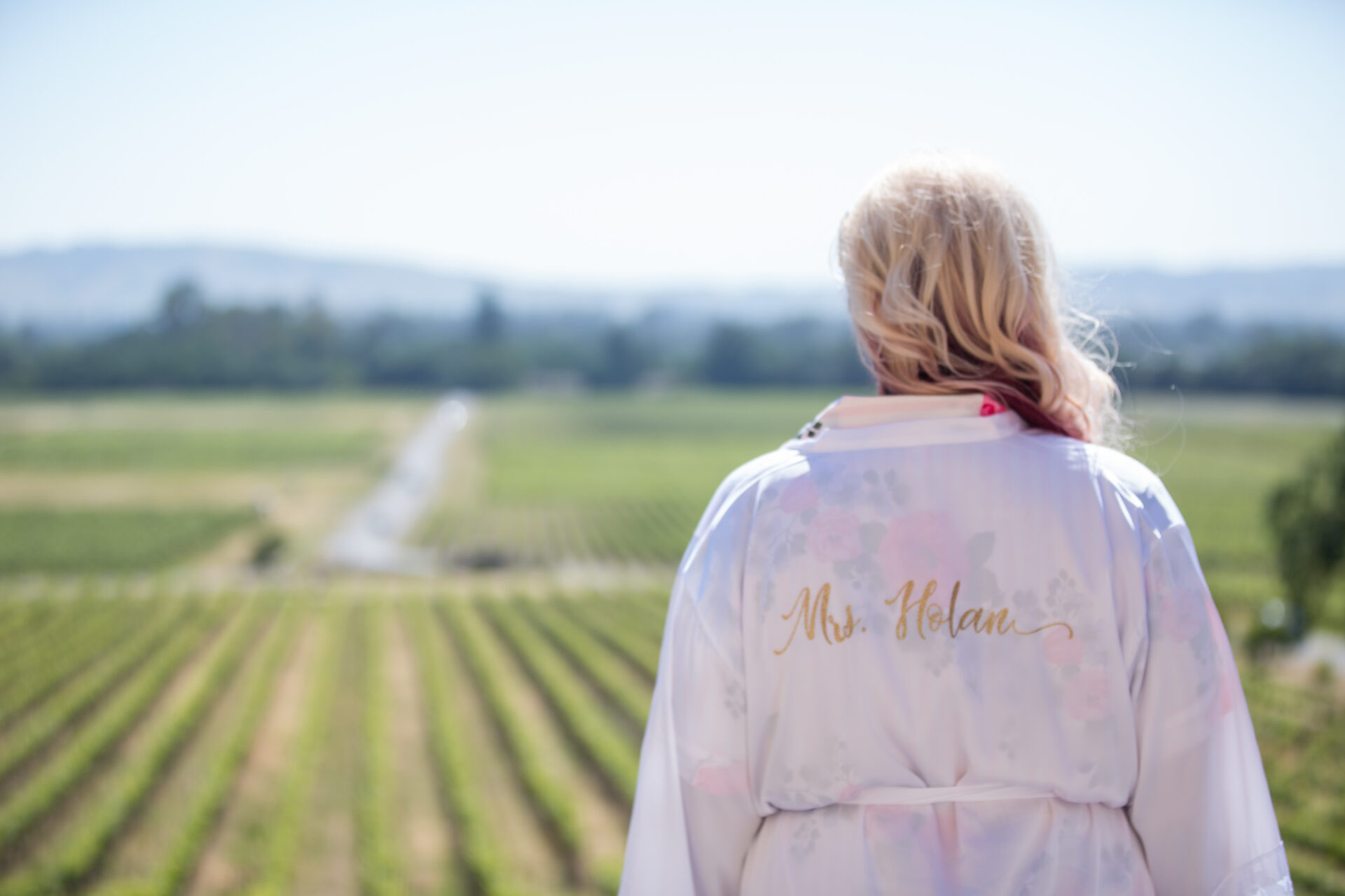 A bride in a robe looking out over a vineyard.