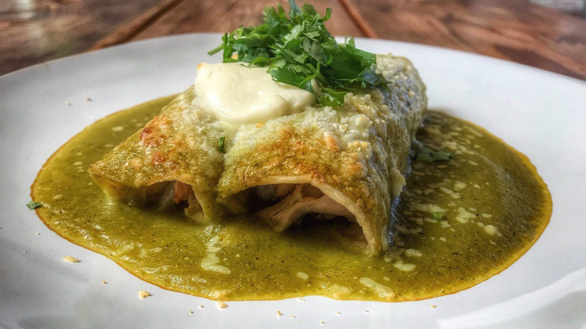 Gourmet chicken enchiladas with green sauce on a white plate.
