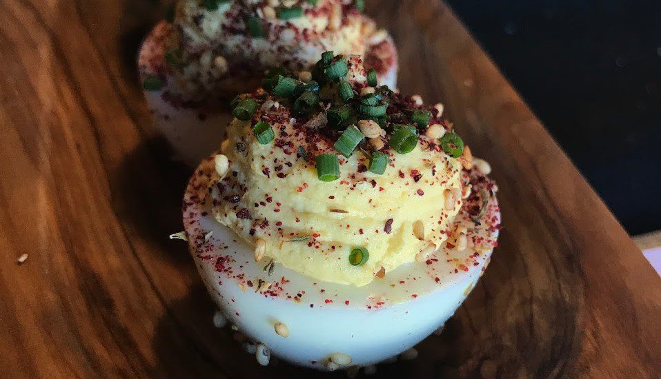Three deviled eggs on a wooden plate.