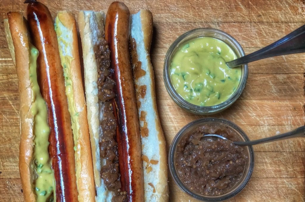 Two hot dogs with mustard and mustard on a wooden cutting board.