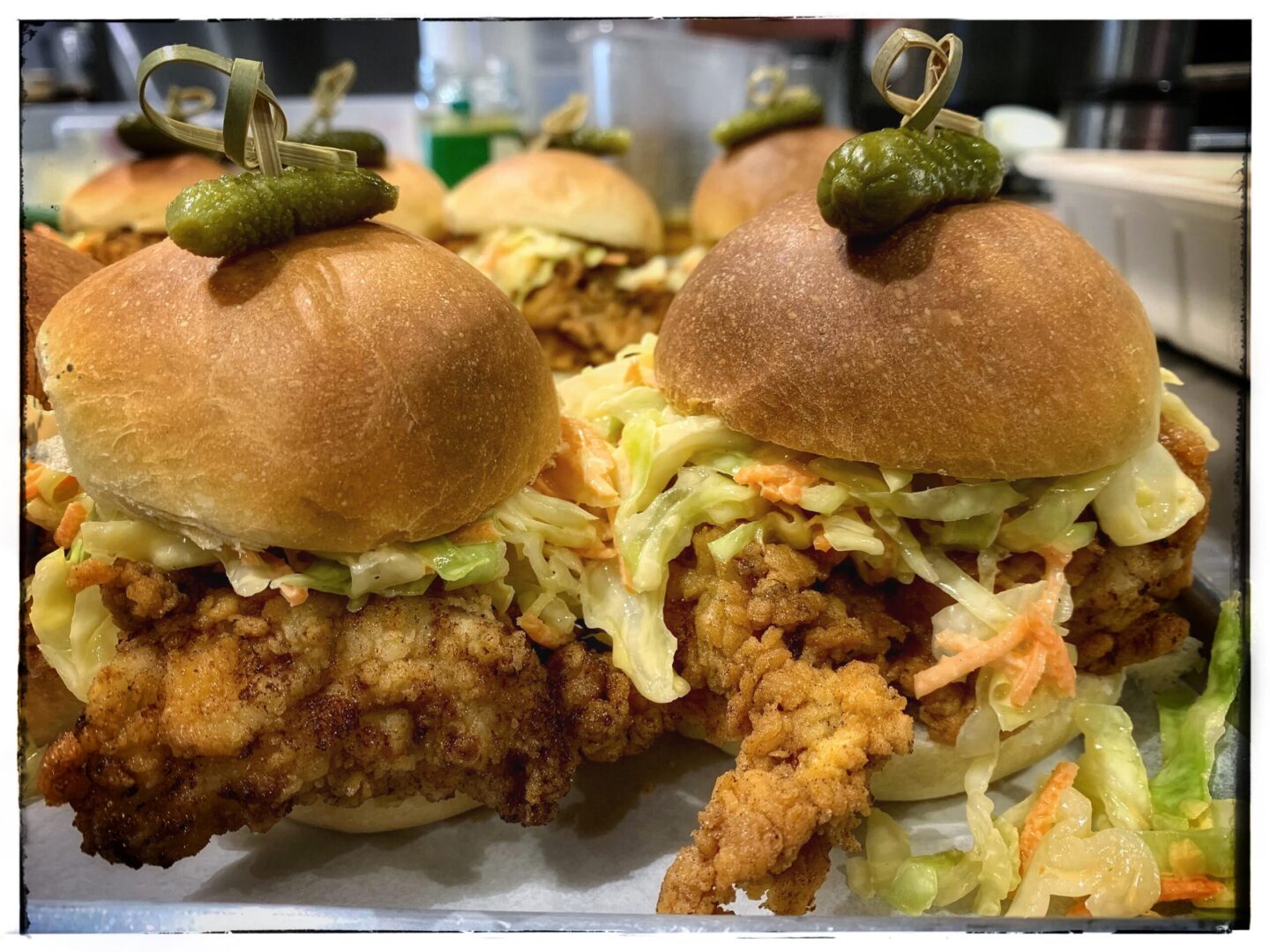 A tray of chicken sliders with coleslaw and pickles.