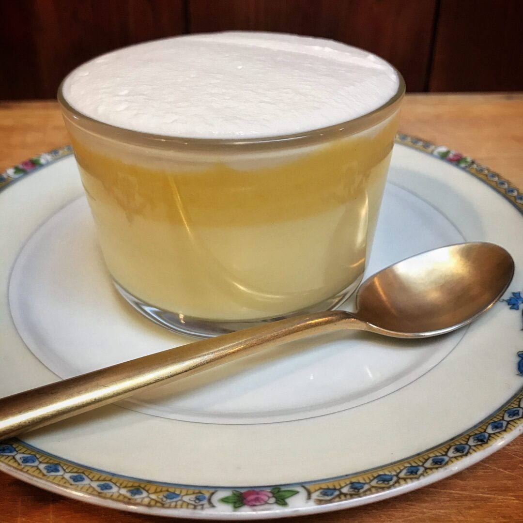 A cup of lemon custard on a plate with a spoon.