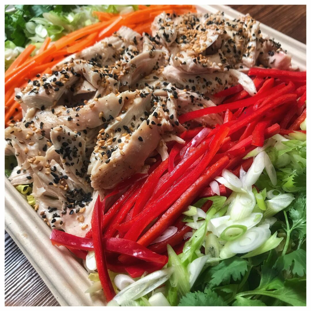 A box with chicken, carrots, lettuce and sesame seeds.