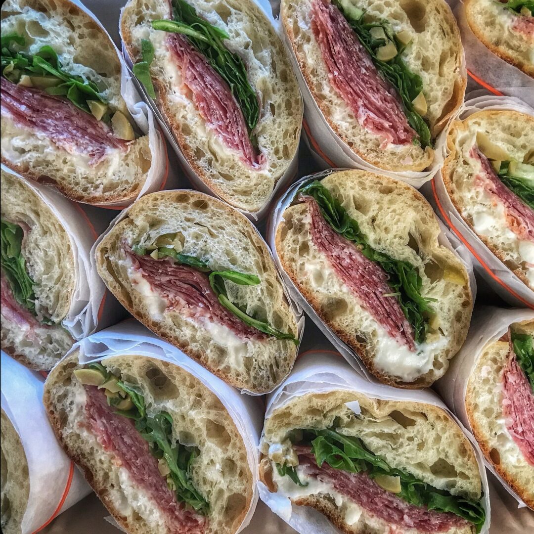 A box of sandwiches with meat and spinach.