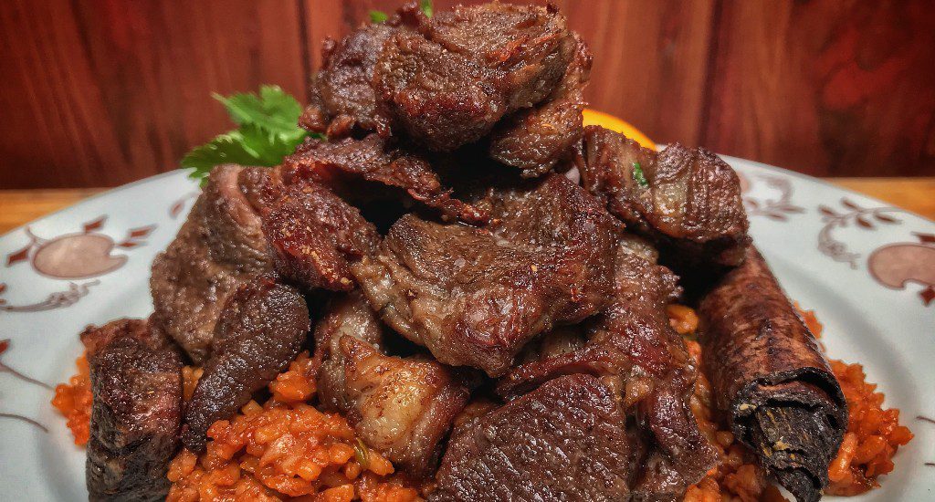 A plate of meat and rice on a wooden table.