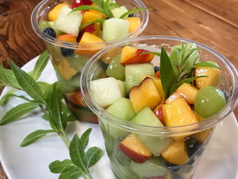 Two cups of fruit salad on a plate with sprigs of sage.